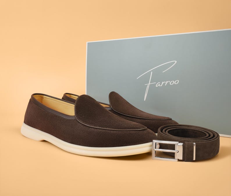 May include: A pair of brown suede loafers with white soles and a matching brown belt with a silver buckle. The items are displayed with a box that has the brand name "Farroo" on it.