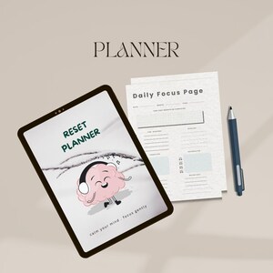 Peut inclure: Une tablette numérique affichant un "Reset Planner" avec un cerveau de dessin animé portant un casque. Une "Daily Focus Page" et un stylo bleu sont à côté de la tablette. Le mot "PLANNER" est en haut.