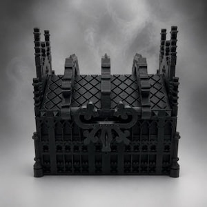 Könnte beinhalten: Eine mattschwarze Aufbewahrungsbox mit komplexen architektonischen Details, darunter ein rautenförmiges Dach, spitzbogige Fenster und dekorative Fialen. Die Vorderseite zeigt einen zentralen, verzierten Verschlussmechanismus.