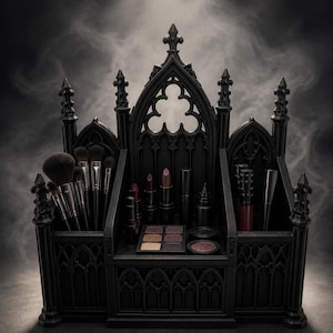 Könnte beinhalten: Ein schwarzer Make-up-Organizer in Form einer Kathedrale mit Spitzbögen und Türmen. Der Organizer enthält mehrere Make-up-Pinsel im linken Fach, während die mittleren und rechten Bereiche verschiedene Lippenstifte, eine Palette und Behälter aufnehmen.