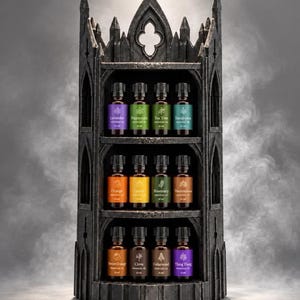 Peut inclure: Un présentoir gris foncé à trois niveaux en forme de tour gothique avec des arches pointues. Il contient douze petits flacons en verre ambré d'huiles essentielles, chacun avec un bouchon noir et une étiquette colorée avec du texte.