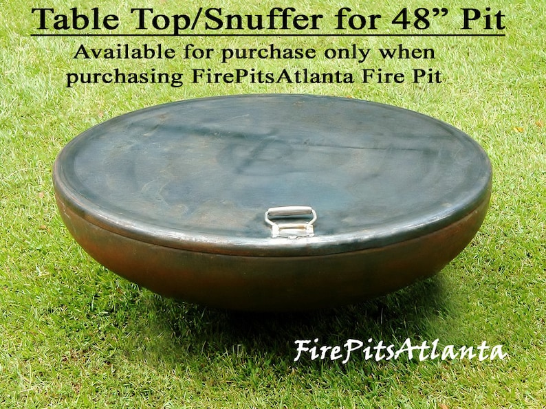 May include: A round, metal table top or snuffer for a 48 inch fire pit. The top is dark gray with a silver handle. The top is sitting on green grass.