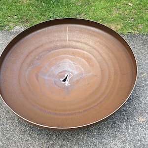 May include: A large, round, rusty metal fire pit with a small hole in the center.