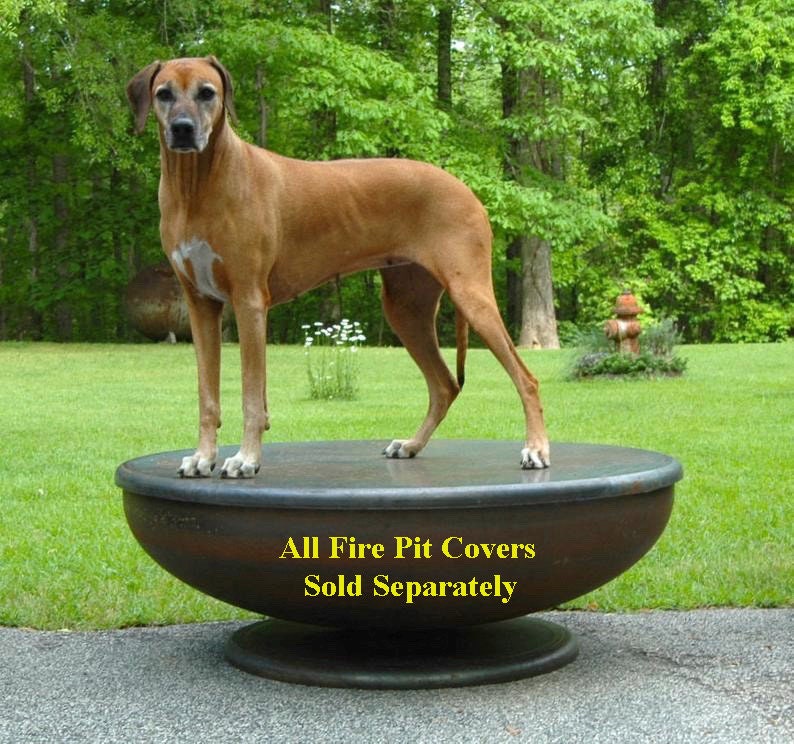 Op de afbeelding: Een bruine hond staat op een grote, ronde, metalen vuurplaatsdeksel. Het deksel staat op een voetstuk. De tekst "All Fire Pit Covers Sold Separately" staat op het deksel gedrukt.