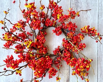 May include: A red and yellow berry wreath with a rustic wooden background.