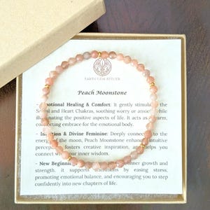 May include: A beaded bracelet made of faceted peach moonstone spheres with small gold-toned metal spacers. The bracelet is displayed on a white card inside a gold-colored box, featuring the text Earth Gem Atelier and Peach Moonstone.