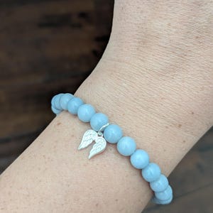 Puede incluir: Una pulsera de cuentas azul claro con un dije plateado de alas de &aacute;ngel. La pulsera est&aacute; hecha de cuentas redondas y lisas. La pulsera se lleva en la mu&ntilde;eca.