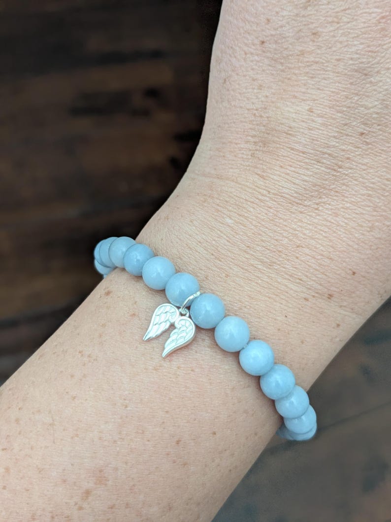 Puede incluir: Una pulsera de cuentas azul claro con un dije plateado de alas de &aacute;ngel. La pulsera est&aacute; hecha de cuentas redondas y lisas. La pulsera se lleva en la mu&ntilde;eca.