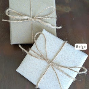 Puede incluir: Dos cajas de regalo, una marr&oacute;n y otra beige, atadas con lazos de cuerda. Las cajas est&aacute;n envueltas en papel texturizado. Texto en la imagen: Opci&oacute;n de envoltorio de regalo disponible al finalizar la compra. Elecci&oacute;n de color marr&oacute;n o beige.