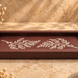 May include: A rectangular dark brown tray with a smooth, matte finish. The interior base of the tray features two white, detailed botanical fern leaf prints positioned horizontally across the center of the flat surface.