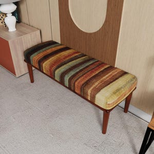 May include: A rectangular bench featuring a cushioned seat upholstered in a multi-colored fabric with horizontal stripes in shades of orange, brown, green, and yellow. The bench is supported by four tapered wooden legs in a dark brown finish.