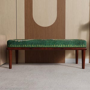 May include: A mid-century modern bench with a rectangular green patterned cushion and dark brown wooden legs. The bench is set against a neutral-toned wall with a decorative design.