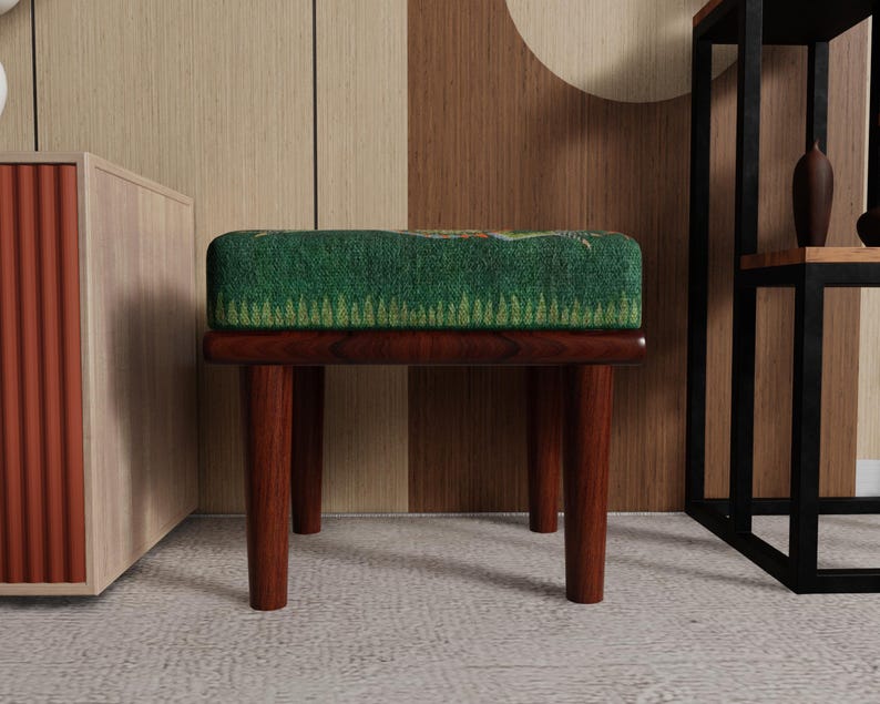 May include: A small, wooden stool with a rectangular, green patterned cushion. The legs are dark brown and angled. The cushion has a forest-like design. The stool is a decorative furniture piece.