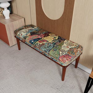 May include: A rectangular bench with a patterned cushion in blue, green, pink, and yellow. The bench has a dark brown wooden frame and legs. The bench is approximately 122 cm long.