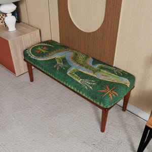 Puede incluir: Banco rectangular con una parte superior tapizada verde con una ilustración de un caimán en tonos azules, verdes y naranjas. El banco tiene un marco y patas de madera oscura. Mide unos 120 cm de largo.