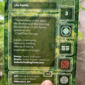 Puede incluir: Una tarjeta coleccionable rectangular con un fondo de bosque verde. La tarjeta presenta el texto Life Family, una cita de Chief Dan George y cr&eacute;ditos para Envoy Delvin Solkinson, Remix Shaun Friesen y la artista Mindy Eva Ouellet.