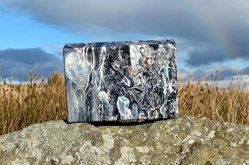 Puede incluir: Un bloque rectangular que presenta una ilustraci&oacute;n detallada en blanco y negro con numerosas figuras superpuestas, incluyendo rostros humanos, animales y elementos celestiales, en un estilo de alto contraste con l&iacute;neas blancas.