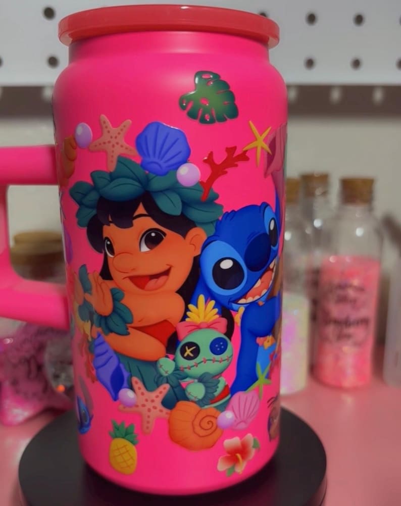 May include: A bright pink tumbler featuring a colorful design of Lilo and Stitch characters, along with tropical elements like seashells, starfish, and flowers. The tumbler has a red rim and handle, and is decorated with various stickers.