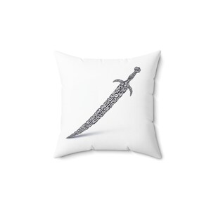 Op de afbeelding: Wit vierkant kussen met een gedetailleerd zwart-grijs zwaardontwerp. Het zwaard heeft een sierlijk patroon en is schuin over het kussen geplaatst. Een decoratief woonaccessoire.