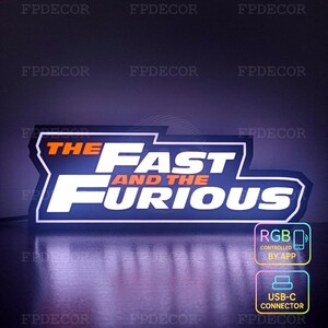 May include: A rectangular LED sign featuring the text "THE FAST AND THE FURIOUS" in white and orange against a dark blue background. The sign includes RGB control via app and a USB-C connector.