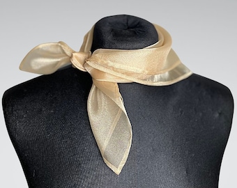 May include: A sheer, light gold scarf tied in a knot on a black mannequin. The scarf is made of a delicate, translucent fabric.