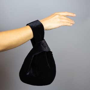 May include: A black velvet bag with a knotted handle. The bag is being held by a hand.