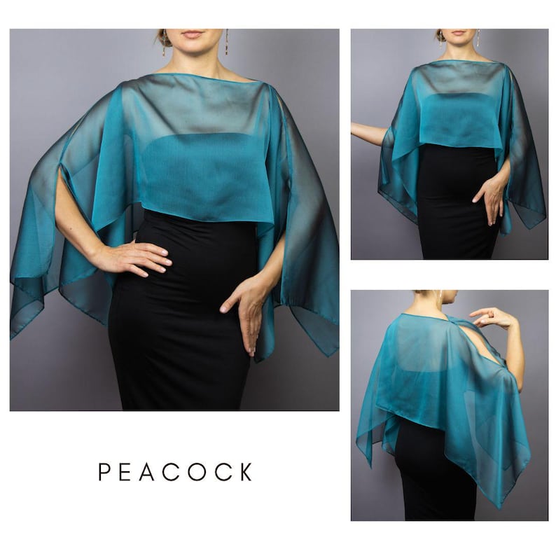 K&ouml;nnte beinhalten: Ein t&uuml;rkisblaues, transparentes Cape mit Bootsausschnitt, &uuml;ber einem t&uuml;rkisfarbenen Oberteil und einem schwarzen Kleid. Das Cape hat ein flie&szlig;endes, offenes Design mit weiten &Auml;rmeln. Das Wort "PEACOCK" ist unten im Bild in Wei&szlig; gedruckt.