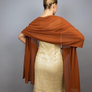 May include: A rust-colored sheer shawl draped over a gold lace dress.