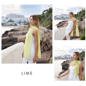 May include: A lime green scarf draped over a white dress. The scarf is a light, flowing fabric. The word "LIME" is printed in white at the bottom of the image. The background shows a coastal landscape with buildings and the ocean.