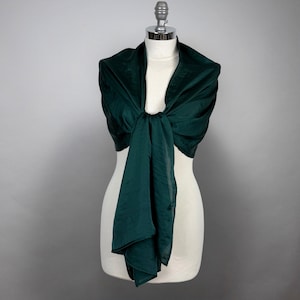 May include: A dark green silk scarf draped over a white mannequin. The scarf is tied in a knot at the front and the ends are hanging down.