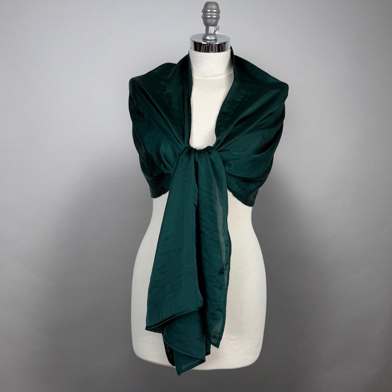 May include: A dark green silk scarf draped over a white mannequin. The scarf is tied in a knot at the front and the ends are hanging down.