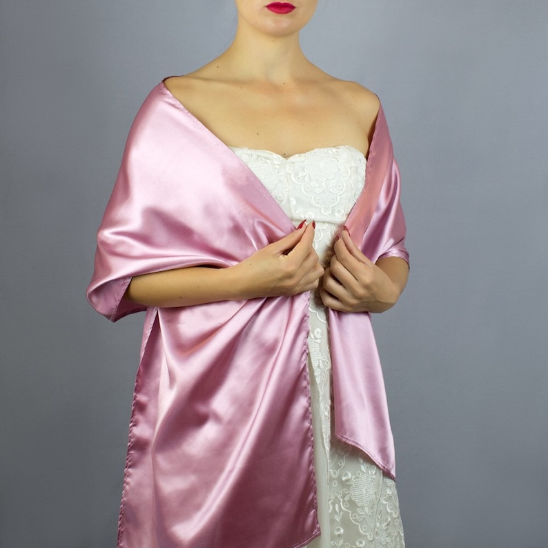 May include: A pink satin shawl draped over a person's shoulders. The shawl is a simple, elegant design and would be a great addition to any formal outfit.