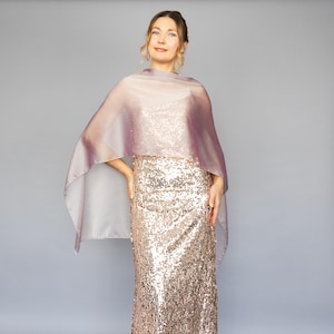 May include: A woman wearing a sequined gold dress with a sheer, light purple and grey shawl.