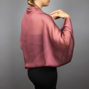May include: A sheer, mauve-coloured shawl with a flowing, draped design. The shawl is made of a lightweight fabric and has a soft, delicate feel.
