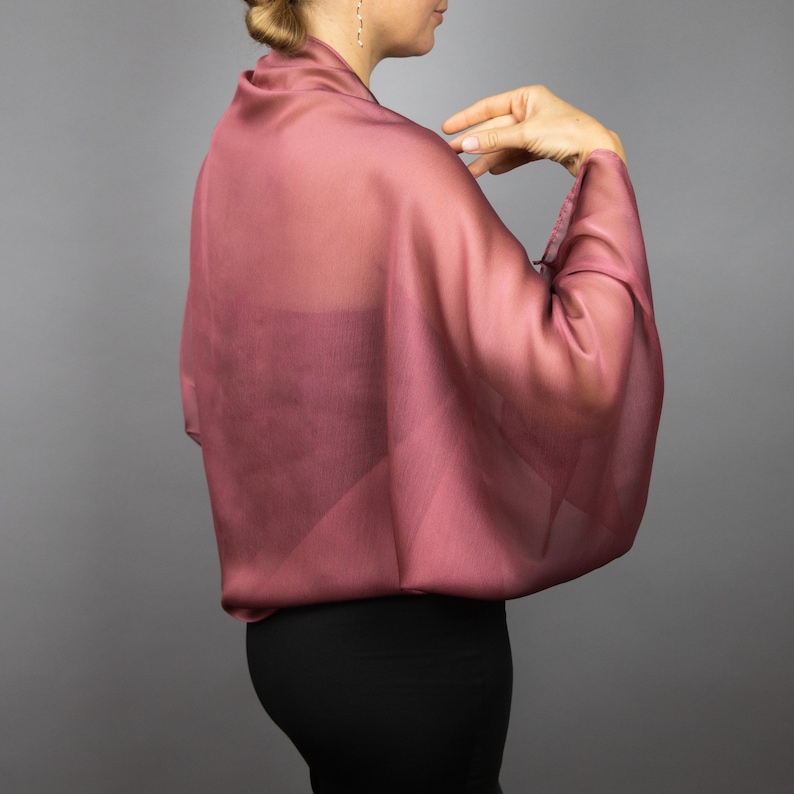 May include: A sheer, mauve-coloured shawl with a flowing, draped design. The shawl is made of a lightweight fabric and has a soft, delicate feel.