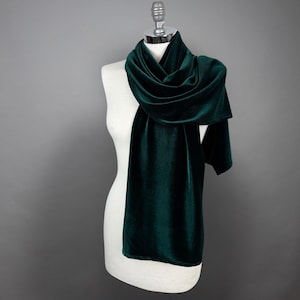 Op de afbeelding: Een donkergroene fluwelen sjaal gedrapeerd over een wit mannequin. De sjaal is lang en vloeiend, met een zachte, luxe textuur.