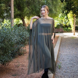 Könnte beinhalten: Eine Frau trägt ein langes, fließendes, durchsichtiges, olivgrünes Kleid mit einem schwarzen Tanktop darunter. Sie steht auf einem Weg in einem Garten.