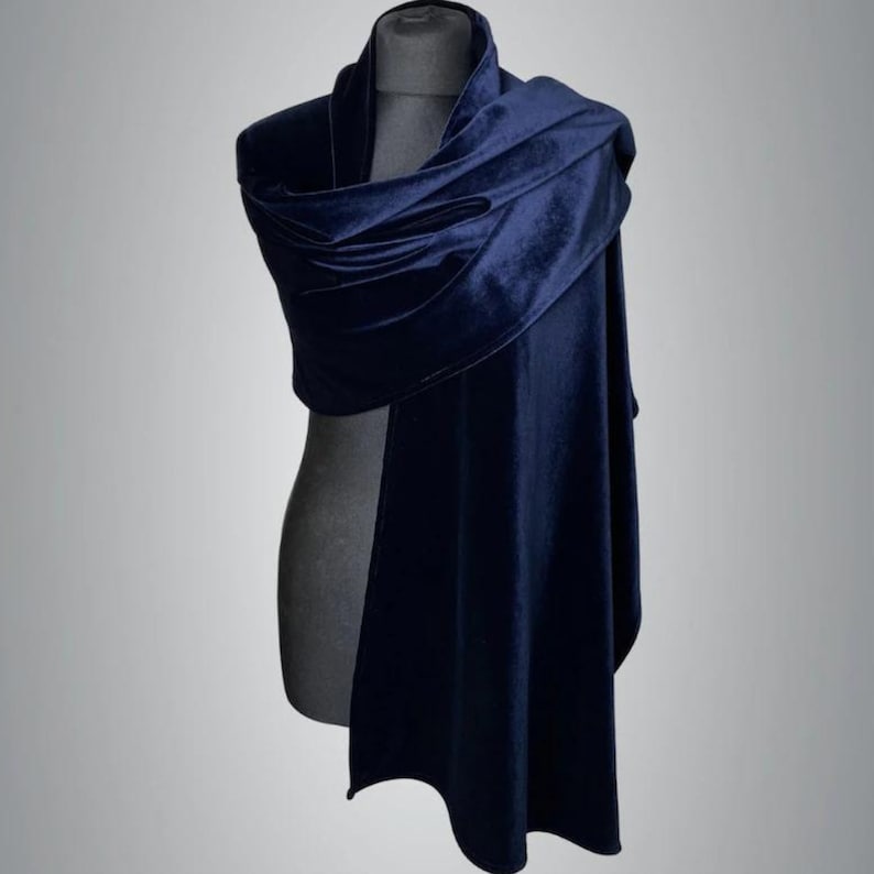 May include: A navy blue velvet shawl draped over a mannequin. The shawl is soft and flowing, with a deep, rich color. The fabric has a subtle sheen, and the design is simple and elegant.