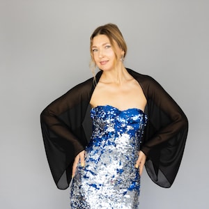 May include: A woman wearing a black sheer shawl over a blue and silver sequined dress. The shawl has long sleeves and a flowing design.