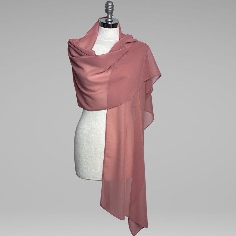 May include: A dusty rose chiffon shawl draped over a white mannequin. The shawl is long and flowing, with a soft, delicate texture.