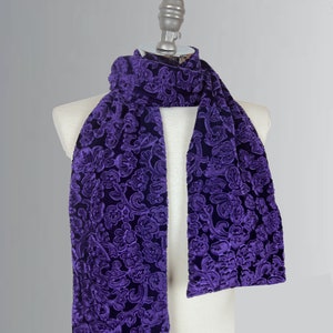 May include: A purple velvet scarf with a floral pattern. The scarf is draped over a white mannequin.