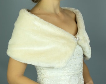 May include: A white faux fur shawl with a crystal brooch. The shawl is draped over the shoulders of a person wearing a white lace dress.