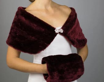 May include: A burgundy faux fur shawl and matching hand muff. The shawl is fastened with a decorative clasp. The set is made of a soft, plush material, perfect for a special occasion or adding a touch of elegance to an outfit.