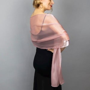 May include: A sheer pink shawl with a subtle shimmer. The shawl is draped over a person's shoulders and is worn with a black dress.