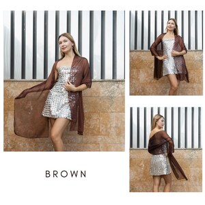 May include: A brown sheer shawl worn with a silver sequined mini dress. The dress is sleeveless. The word "BROWN" is displayed in white block letters at the bottom of the image. The background features a wall and vertical metal bars.