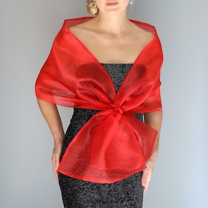 May include: A red sheer shawl with a bow tied in the front. The shawl is made of a lightweight, flowing fabric and is perfect for adding a touch of elegance to any outfit.