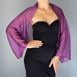 Può includere: Una donna indossa un abito nero senza spalline con uno scialle di chiffon viola. Lo scialle ha un design fluido e drappeggiato e aggiunge un tocco di eleganza all'outfit.