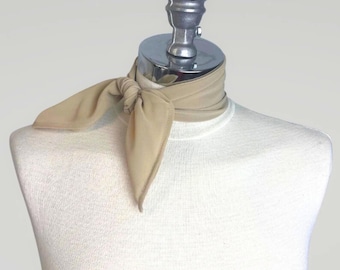 May include: A beige scarf tied around a mannequin's neck. The scarf is made of a soft, lightweight fabric and has a simple, elegant design.