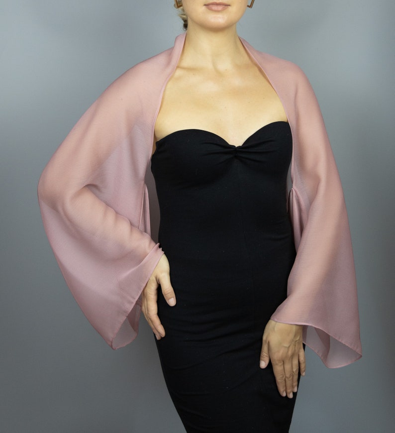 May include: A dusty rose sheer shawl with long, flowing sleeves. The shawl is draped over a person wearing a black strapless dress.