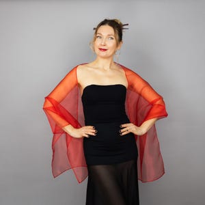 Peut inclure: Un châle rouge en voile drapé sur une personne portant une robe noire sans bretelles. Le châle est fait d'un tissu léger et translucide et a un aspect fluide et élégant.